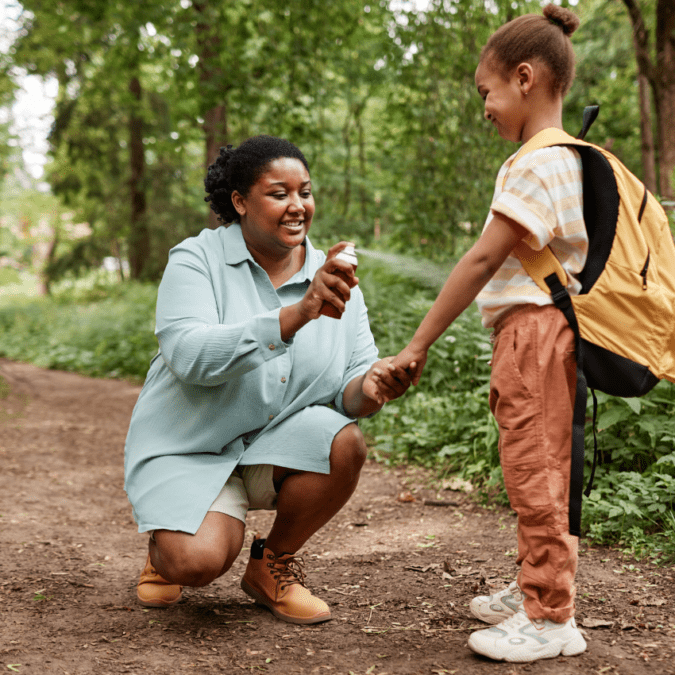 caregiver spraying bug spray on a child in the woods