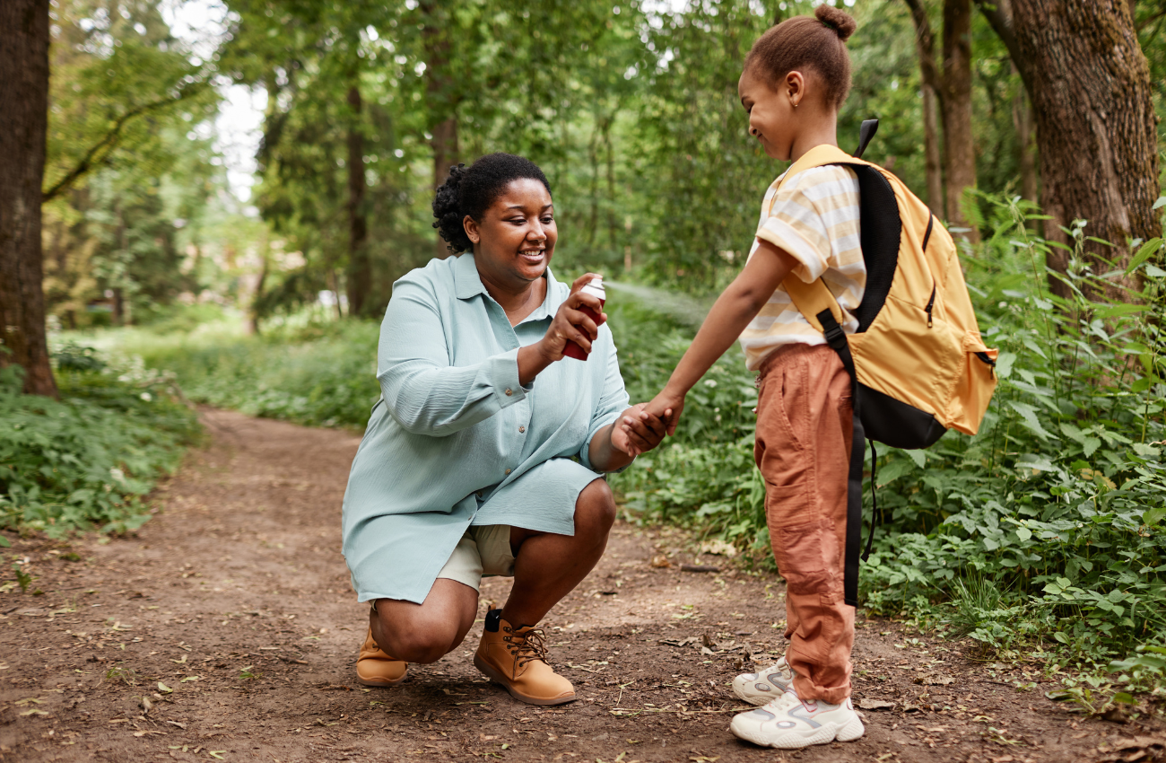 caregiver spraying bug spray on a child in the woods