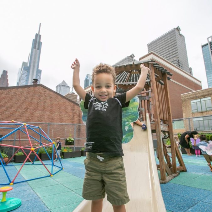 preschool boy playing in outdoor playground city skyline behind him