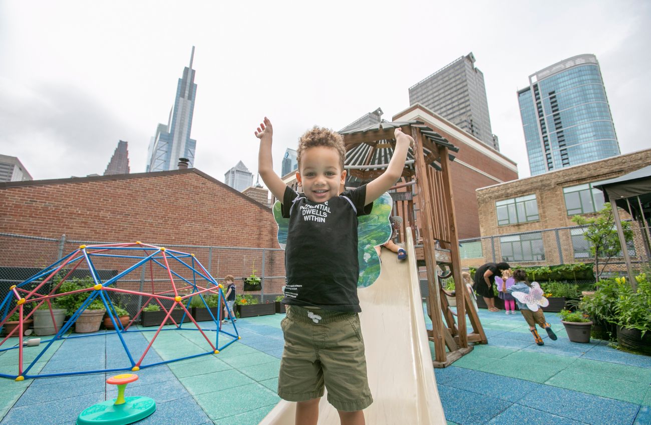 preschool boy playing in outdoor playground city skyline behind him