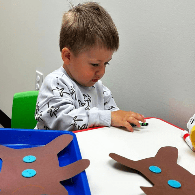 Male toddler doing art at a preschool table.