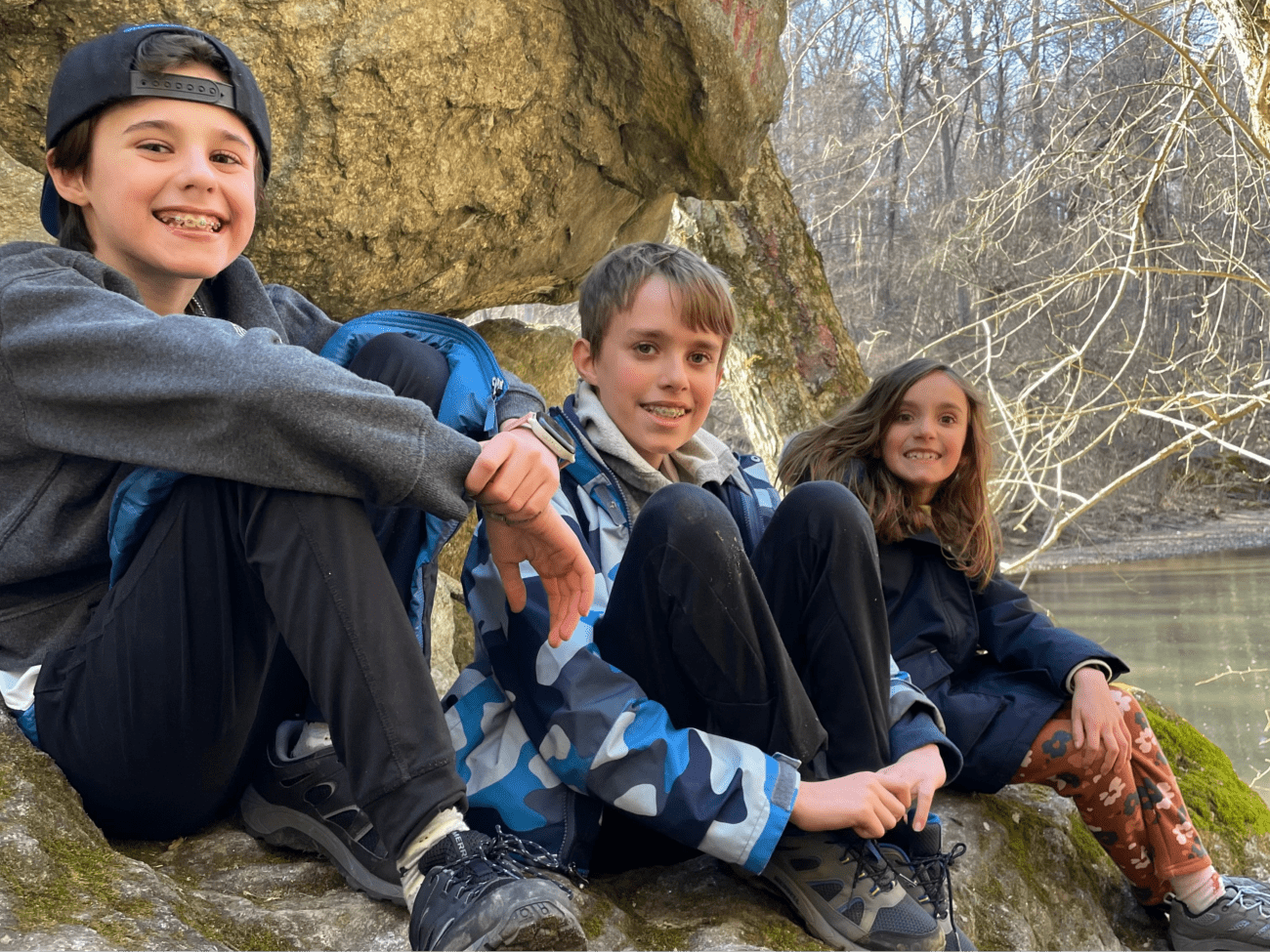 Three siblings sitting against a rock while taking a hike