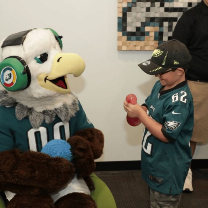 The Philadelphia Eagles mascot sits with a boy playing with a fidget toy.