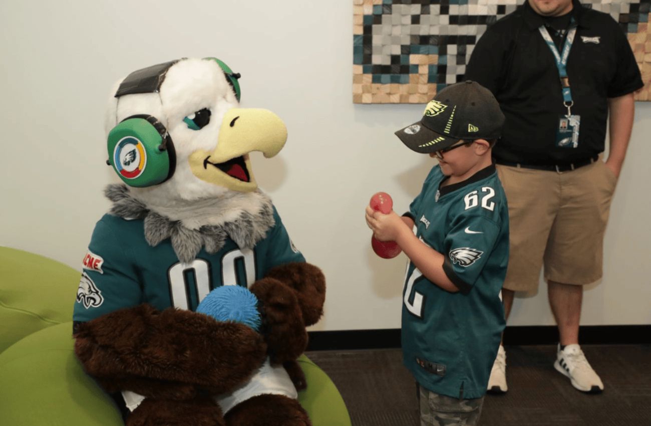 The Philadelphia Eagles mascot sits with a boy playing with a fidget toy.