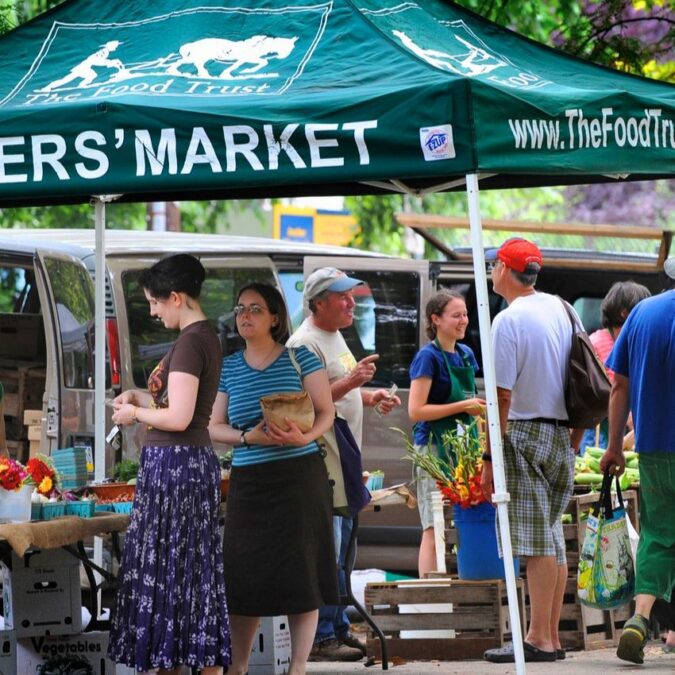 Shoppers surround a green umbrella above a vendor at Clark Park farmers market in Philadelphia.