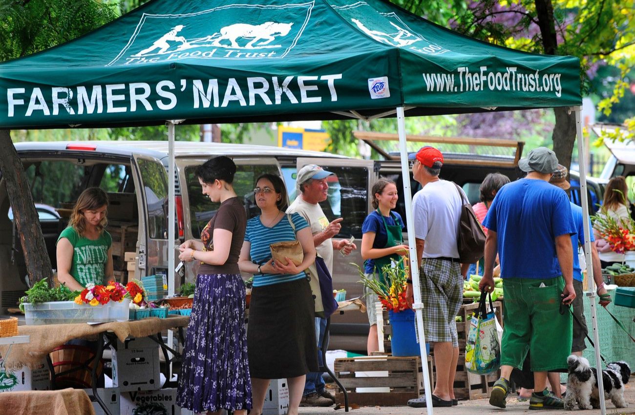 Shoppers surround a green umbrella above a vendor at Clark Park farmers market in Philadelphia.