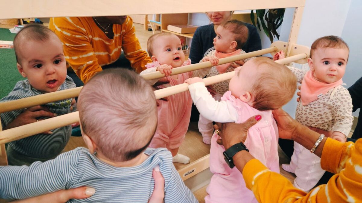 Babies holding themselves up and looking in a mirror.