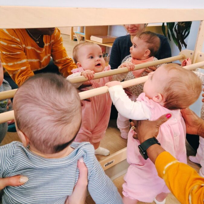 Babies holding themselves up and looking in a mirror.