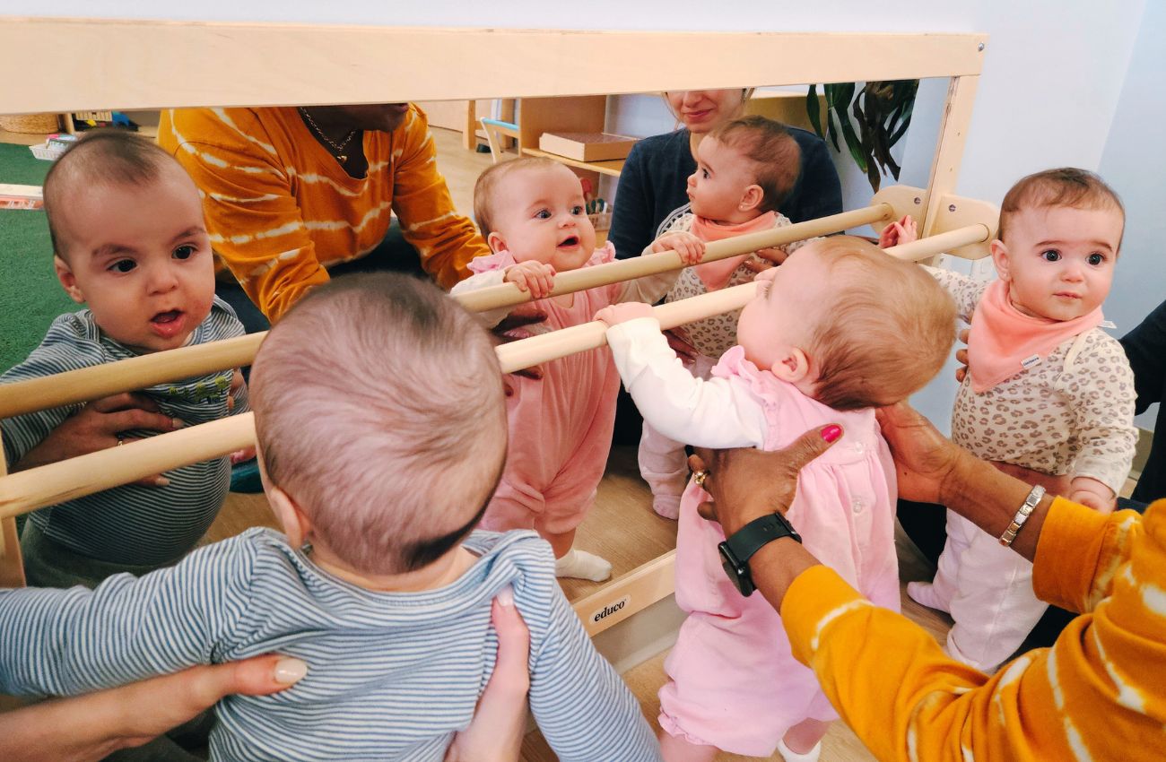 Babies holding themselves up and looking in a mirror.