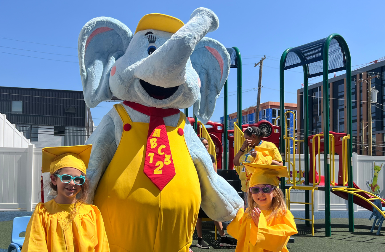 An elephant character posing with two preschool graduates