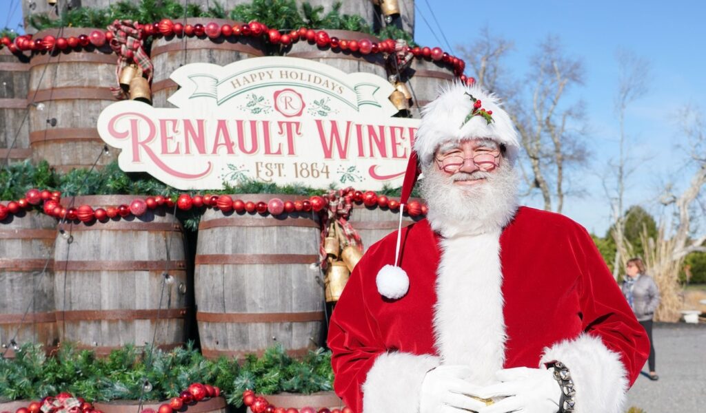 Santa standing in front of a stack of wine barrels that look like a christmas tree