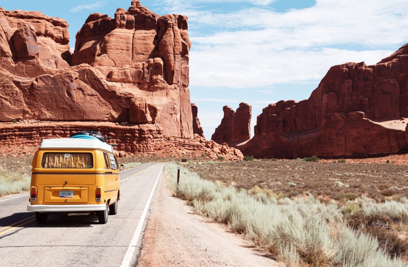 A yellow family van drives an empty road out west from the Family Road Trip Trivia Podcast.