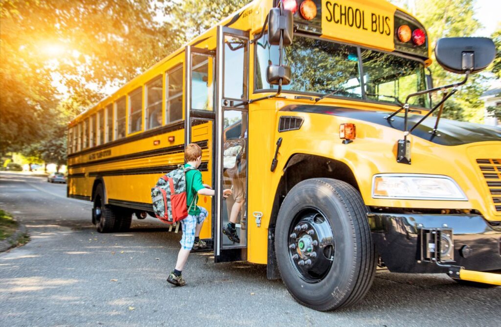A boy steps up to a yellow school bus on a sunny afternoon.
