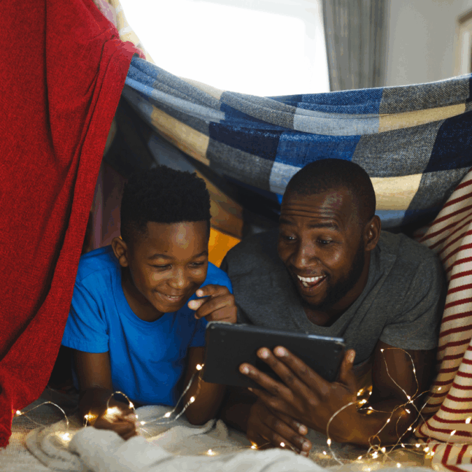 A father and son cozy up in a blanket form with an iPad.