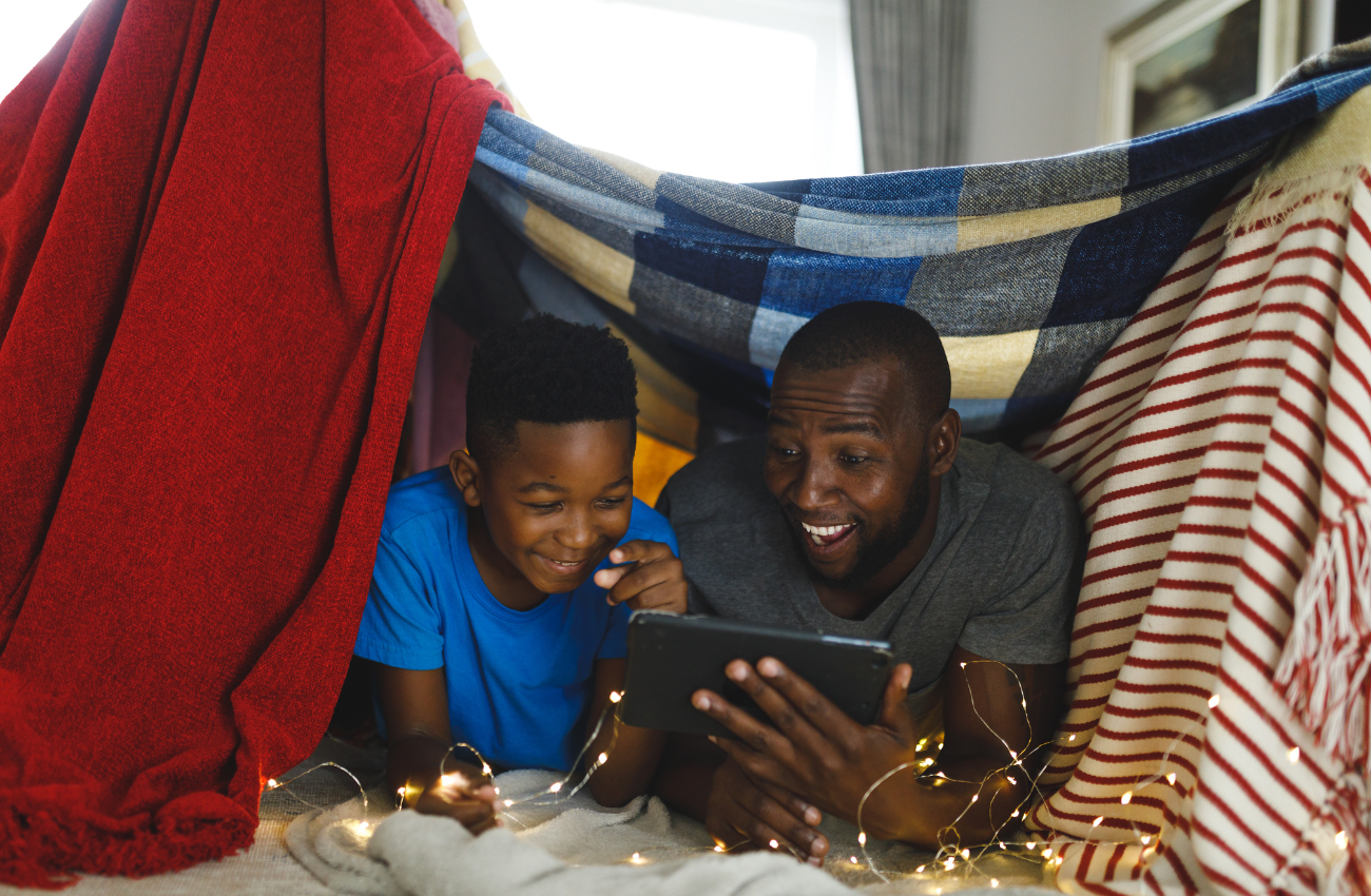A father and son cozy up in a blanket form with an iPad.