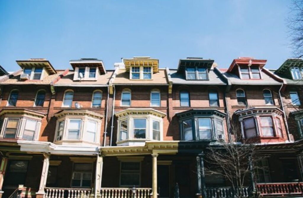 Five, late 19th century row houses in West Philadelphia against a blue sky. 