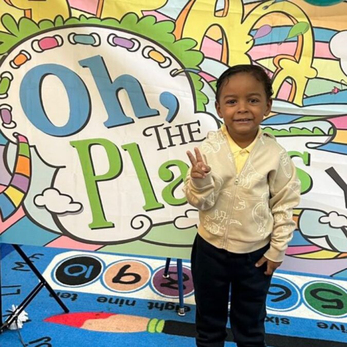 A boy in a free pre-K program in Philly gives the peace sign in front of a Dr. Seuss mural.