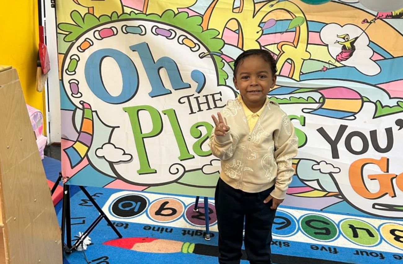 A boy in a free pre-K program in Philly gives the peace sign in front of a Dr. Seuss mural.