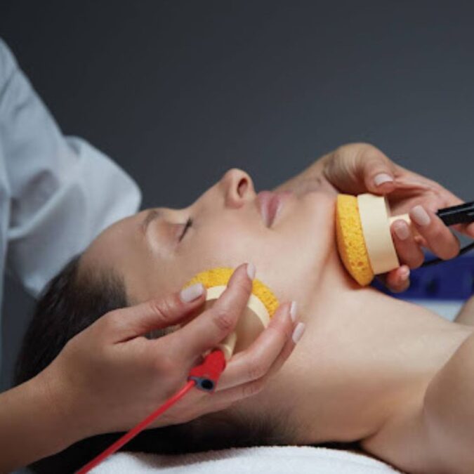 An attendant performs a Philly spa treatment with foam brushes on a woman neck and face.