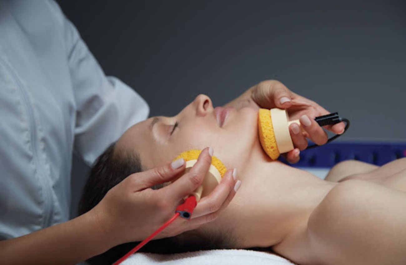An attendant performs a Philly spa treatment with foam brushes on a woman neck and face.