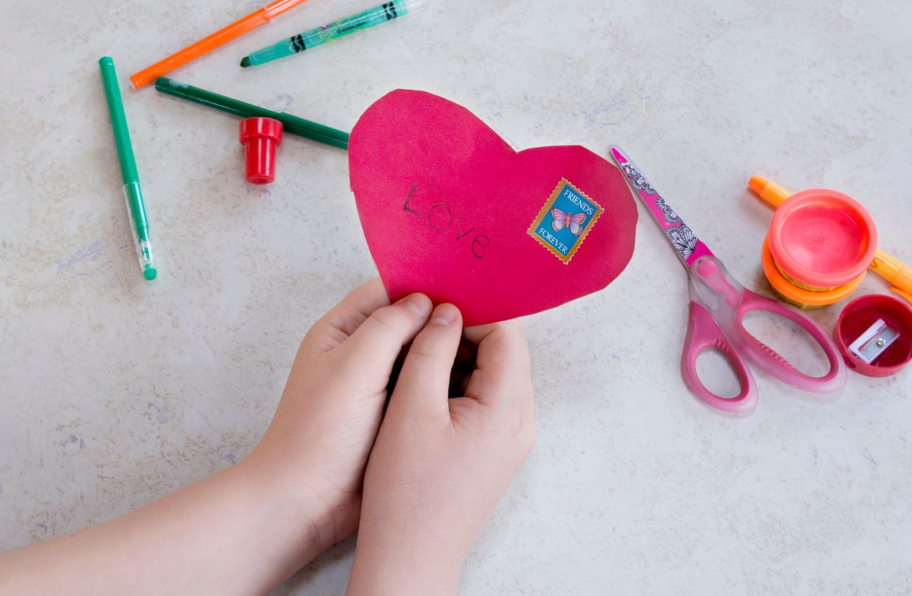 A child's hands hold a red paper heart that says Love for Valentine's Day.