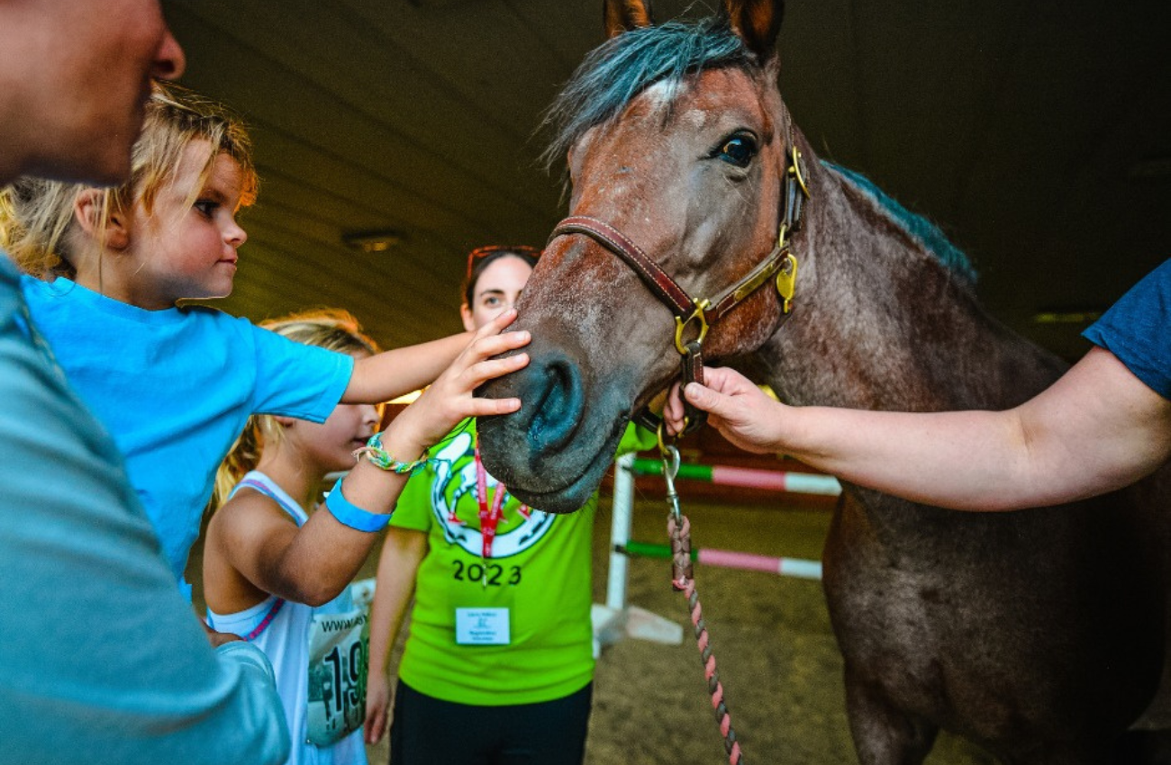 A group of people surround a brown horse held by an adult hand, while two children pat it nose at Thorncroft stables in Malvern, PA.