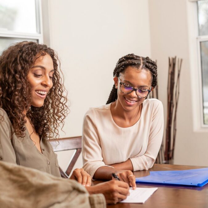A tutor sits beside a teen student at a tab;e