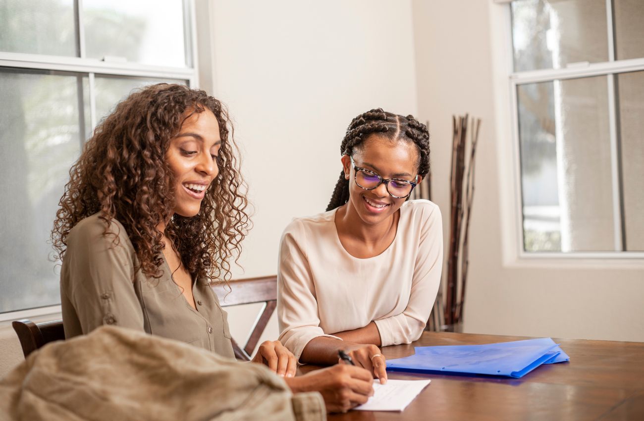 A tutor sits beside a teen student at a tab;e