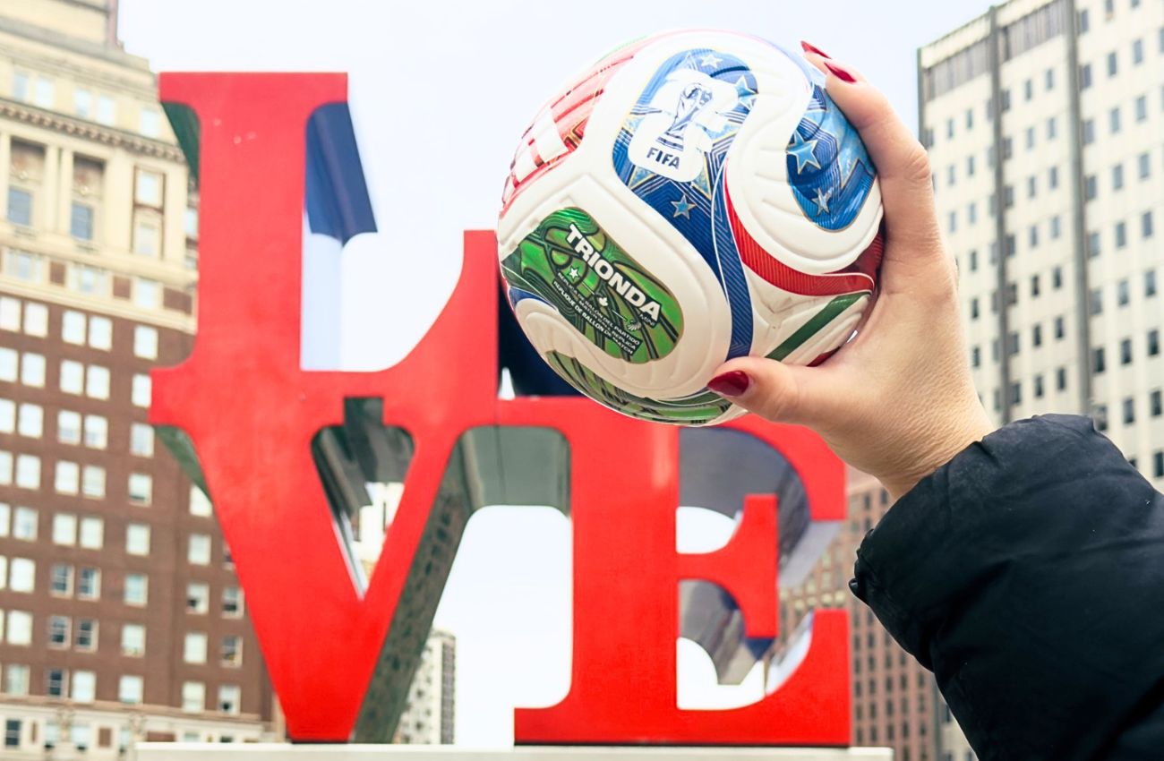 A hand holds a FIFA World Cup 2026 mini soccer ball in front of the LOVE sculpture in Philadelphia.