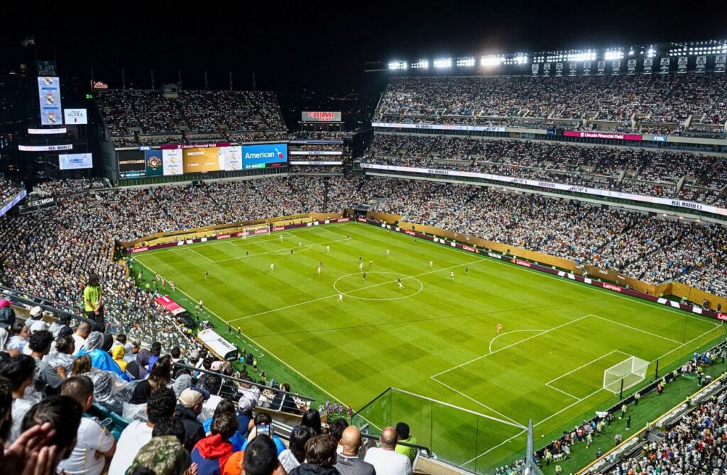 A soccer match takes place on green field surrounded by a stadium packed with fans.