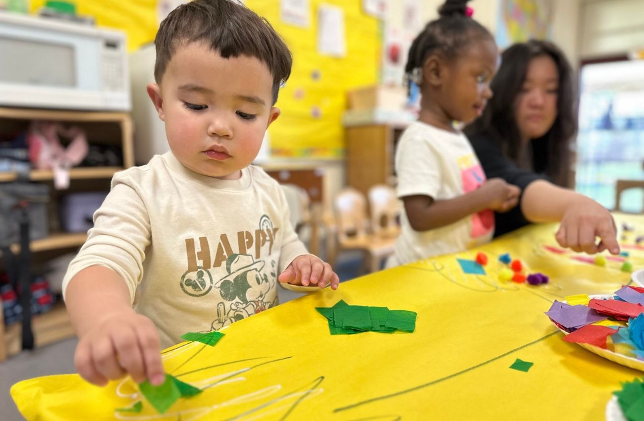 A boy sticks paper cutouts on a bright yellow table pattern at a free Philadelphia Pre-K class.