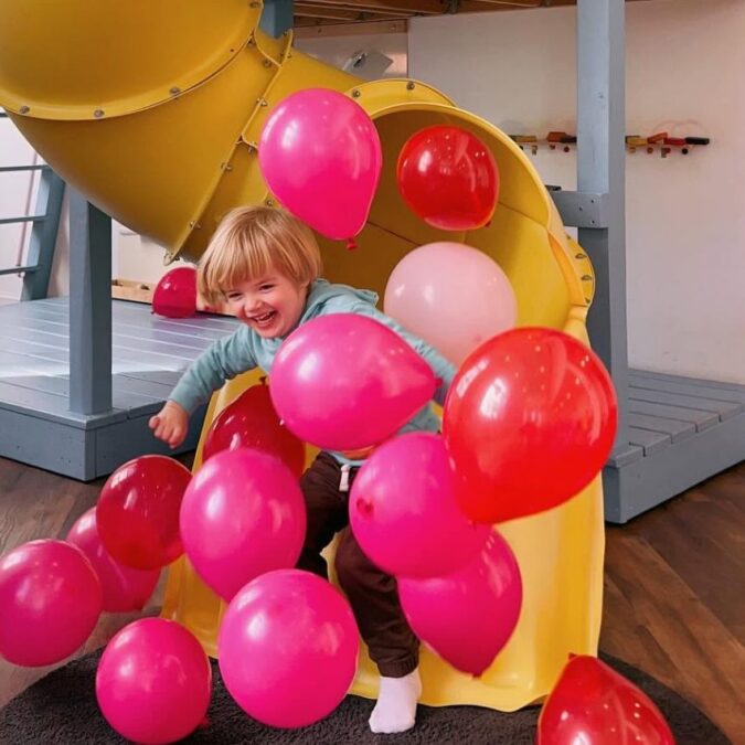 A boy emerges from a yellow slide with lots of pink balloons at Kith + Kin in Philadelphia.