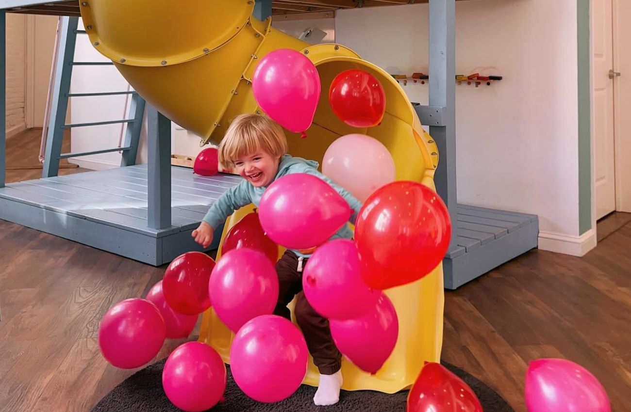 A boy emerges from a yellow slide with lots of pink balloons at Kith + Kin in Philadelphia.
